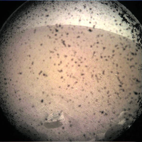 Це перше зображення, зроблене InSight lander на поверхні Марса. У процесі посадки «прозора кришка об’єктива була все ще на місці, щоб захистити його від пилу, який осідає.